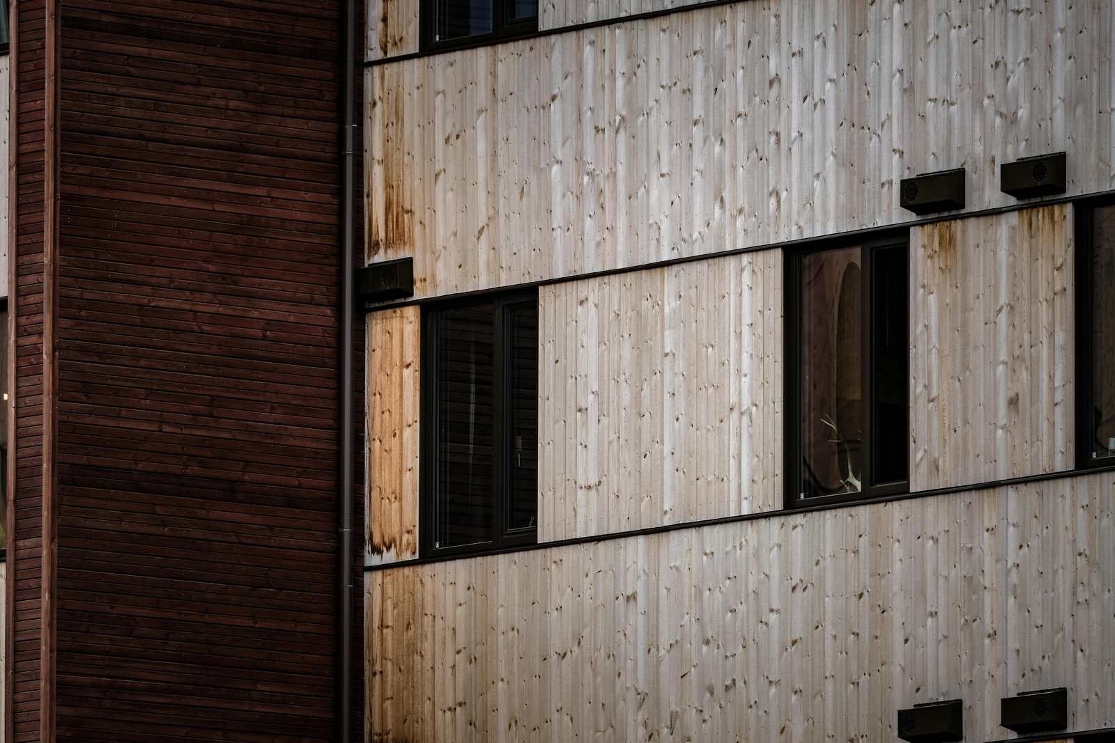 Facade med lodret, gråt og vejrbidt træbeklædning og mørke vinduer
