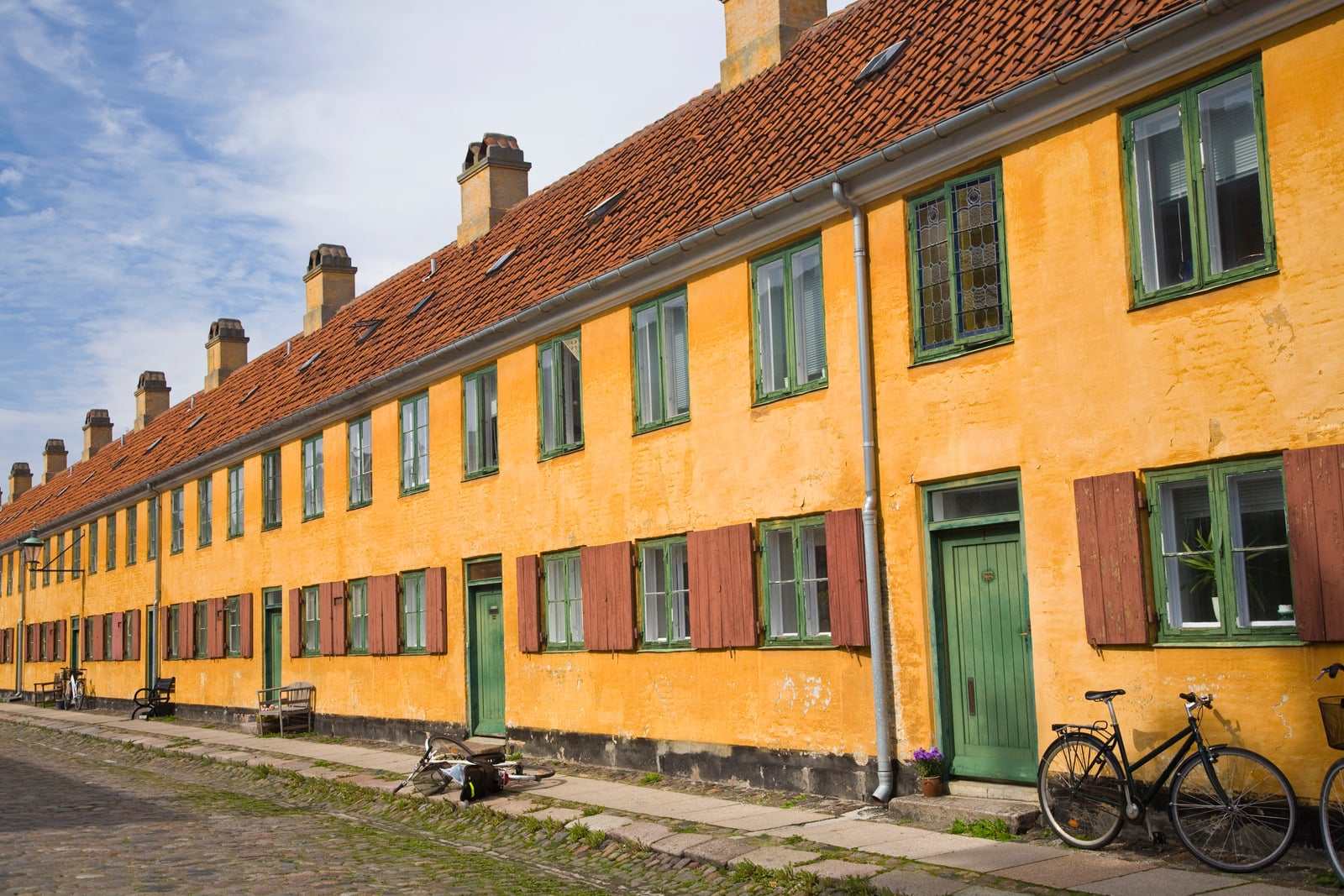 Lang række af okkergule, pudsede rækkehuse med grønne døre og røde tegltage