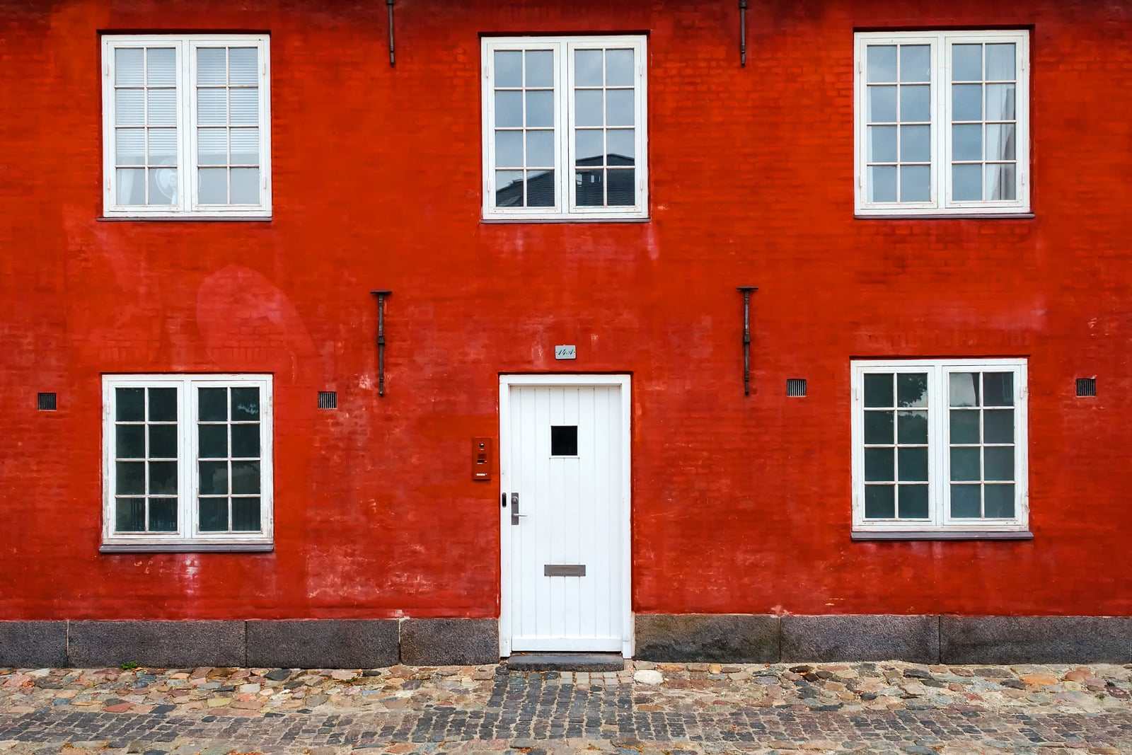 Rødpudset husfacade med hvide vinduer og hvid hoveddør